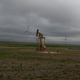 A natural gas pump sits on land next to wind mills, as fracking and wind power are both common sights along the roads, May 10, 2021